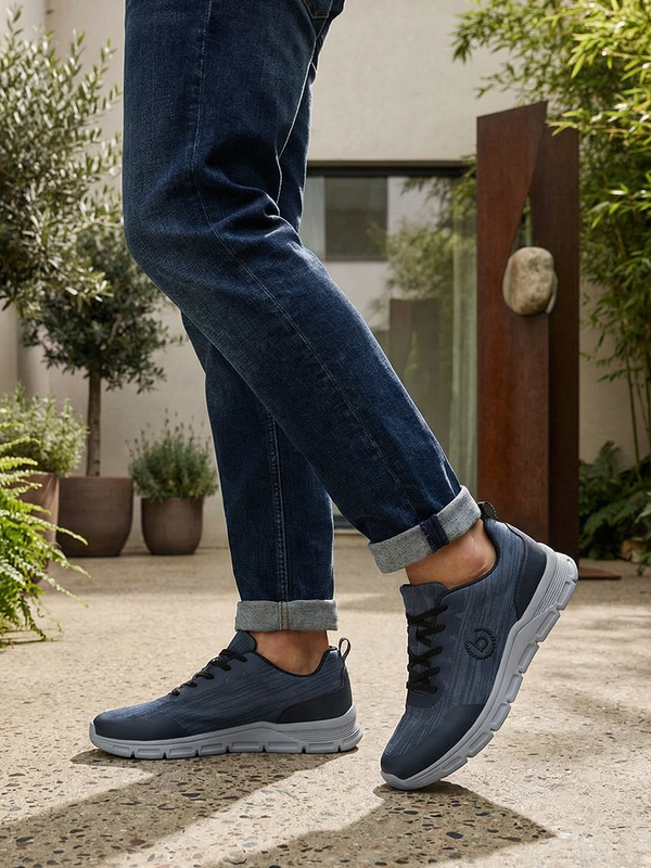 Lifestyle shot of bugatti Nexon blue sneakers with grey soles, worn with blue jeans and rolled cuffs.