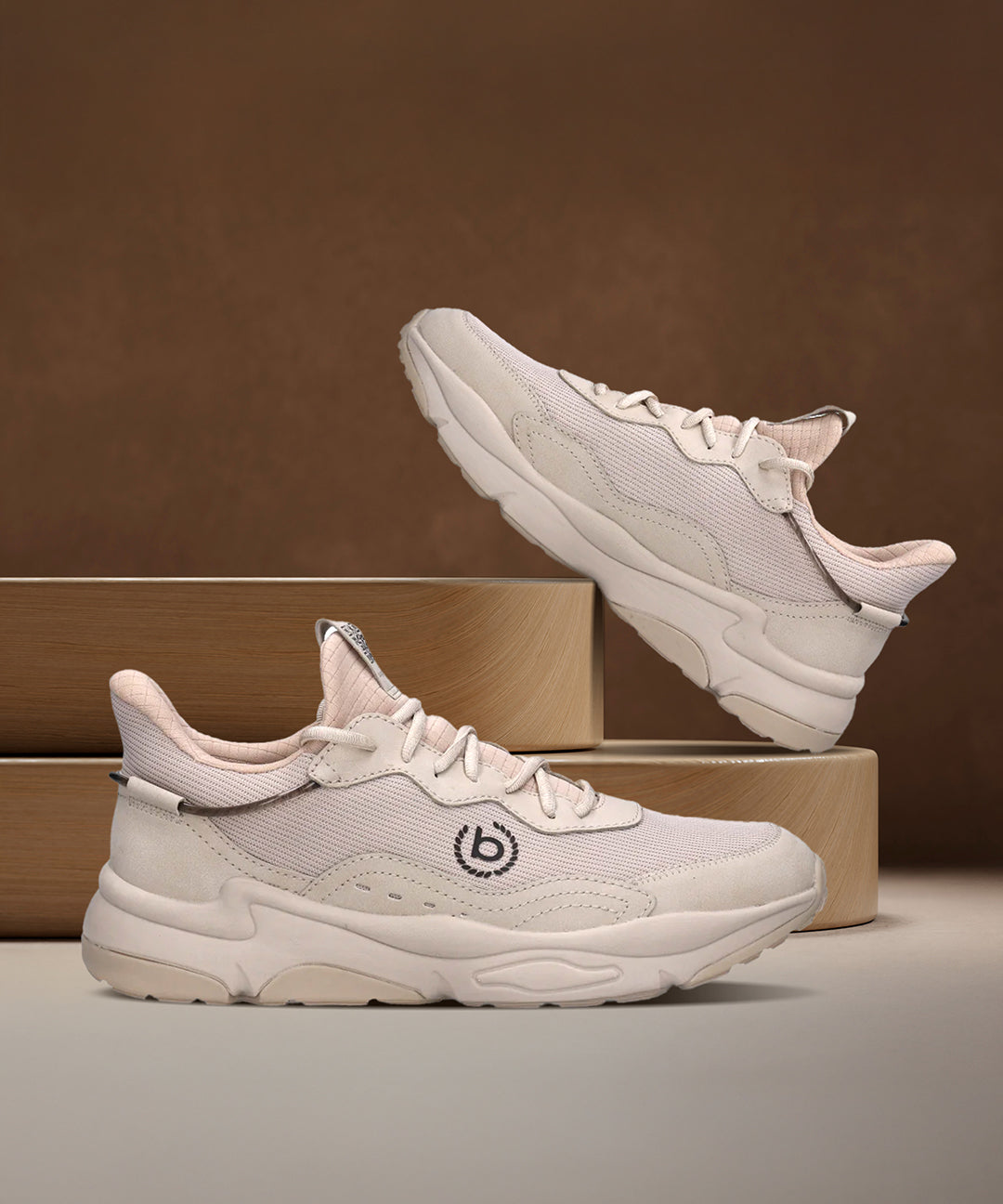 Beige bugatti Adelson Comfort Sneakers with breathable mesh and synthetic suede, presented on wooden display blocks.
