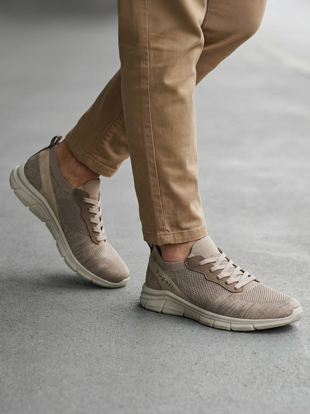 Lifestyle shot of bugatti Soa beige sneakers; a woven knit upper with matching khaki casual pants.
